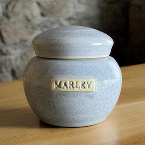 May include: A small, light blue ceramic jar with a lid. The jar has a label that says "MARLKY" in yellow lettering.