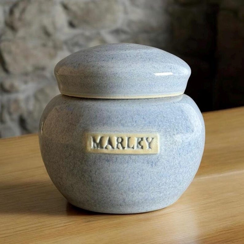 May include: A small, light blue ceramic jar with a lid. The jar has a label that says "MARLKY" in yellow lettering.