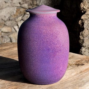 Puede incluir: Un tarro de cerámica morado con tapa. El tarro tiene un acabado moteado y una forma redondeada.