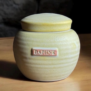 May include: A yellow ceramic jar with a lid and a label that says "Daphne".