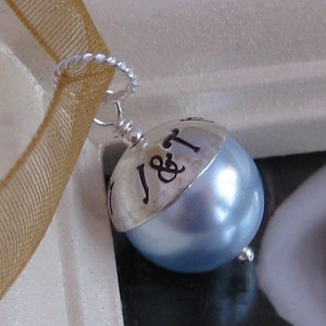 May include: A silver charm with a blue pearl and the inscription "J&T" on the top.