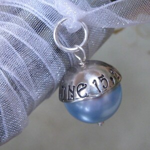 Puede incluir: Un charm de plata con una perla azul y la inscripci&oacute;n "June 15th" en la parte superior.