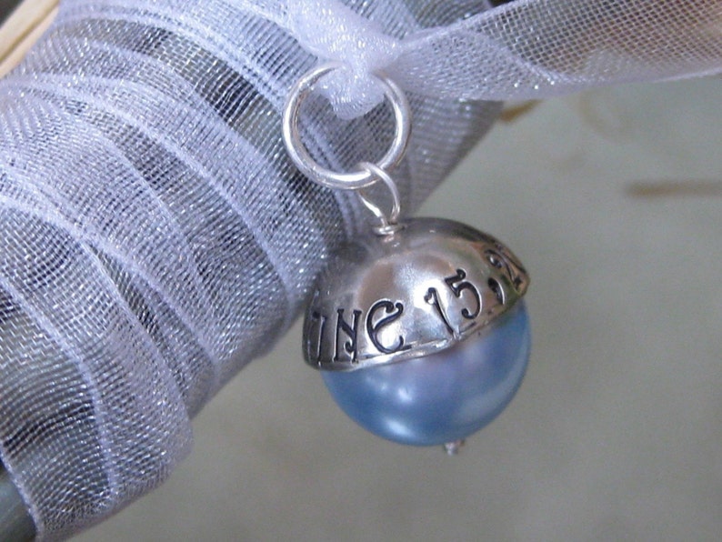 Puede incluir: Un charm de plata con una perla azul y la inscripci&oacute;n "June 15th" en la parte superior.