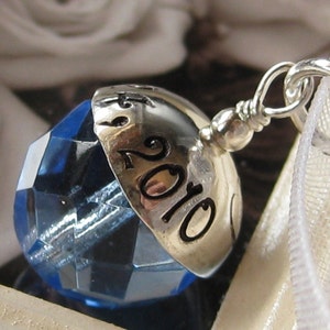 Puede incluir: Un charm de plata con un cristal azul y el a&ntilde;o 2010 grabado en &eacute;l.