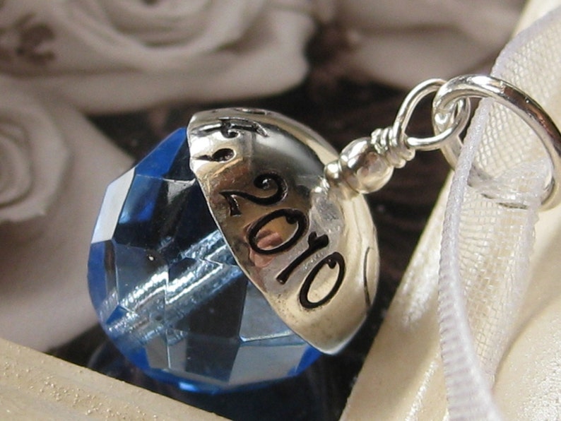 Puede incluir: Un charm de plata con un cristal azul y el a&ntilde;o 2010 grabado en &eacute;l.