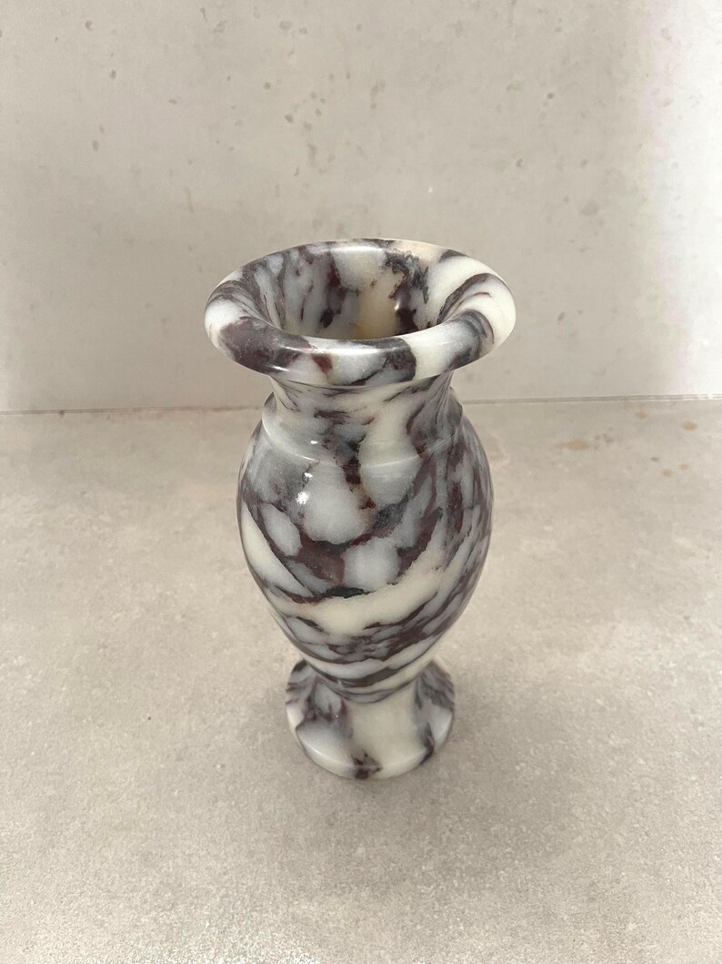 May include: A small, polished stone vase featuring a marbled pattern with deep purple and white veins. The vase has a flared rim, a narrow neck, a rounded body, and a circular base, showcasing a smooth, glossy finish throughout the entire piece.