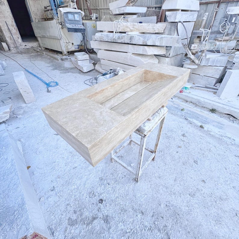 Handmade rectangular beige travertine stone sink with a recessed basin, thick solid edges, and natural stone texture, photographed in a marble workshop before bathroom installation.