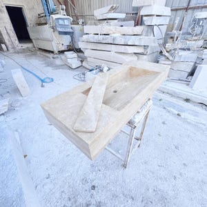 Handmade rectangular beige travertine stone sink with a recessed basin, thick solid edges, and natural stone texture, photographed in a marble workshop before bathroom installation.
