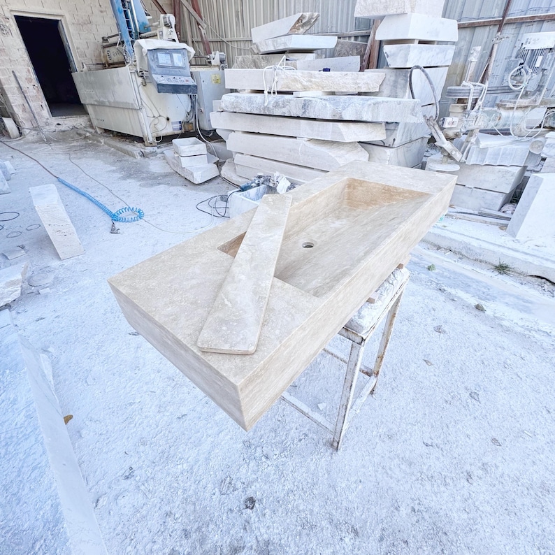 Handmade rectangular beige travertine stone sink with a recessed basin, thick solid edges, and natural stone texture, photographed in a marble workshop before bathroom installation.