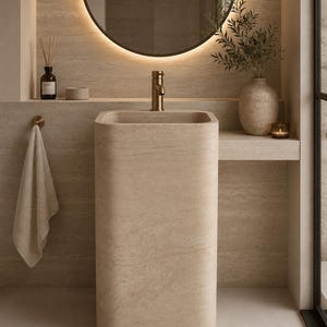 Handmade travertine pedestal sink crafted from natural stone, freestanding bathroom vanity sink with polished finish in a modern luxury bathroom.