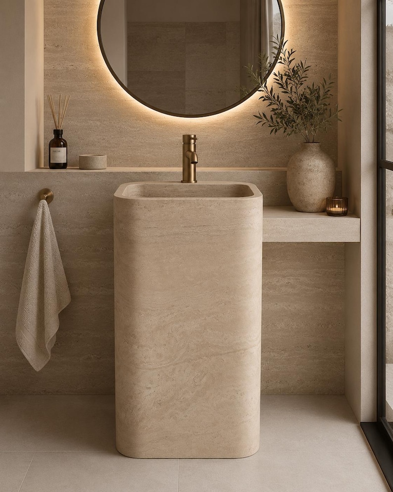 Handmade travertine pedestal sink crafted from natural stone, freestanding bathroom vanity sink with polished finish in a modern luxury bathroom.