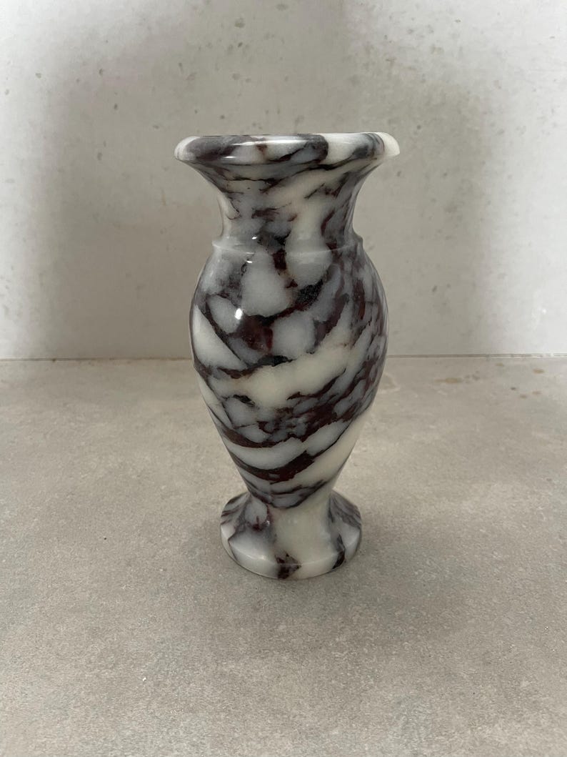 May include: A small, polished stone vase featuring a distinct marbled pattern with swirling veins of deep dark purple and white. The vase has a flared rim, a rounded body, and a circular pedestal base, showcasing a smooth, glossy finish throughout.