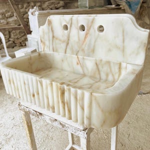 This luxurious Calacatta Gold marble sink with a back panel features a standard drain hole and a striking, elegant design with prominent grey and yellow veins on the front. It can be wall-mounted or countertop-mounted. The front has a fluted design.