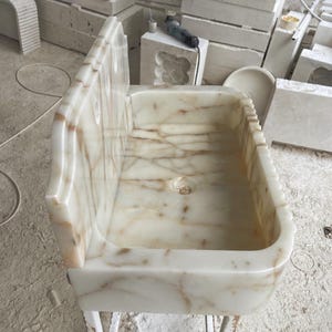This luxurious Calacatta Gold marble sink with a back panel features a standard drain hole and a striking, elegant design with prominent grey and yellow veins on the front. It can be wall-mounted or countertop-mounted. The front has a fluted design.