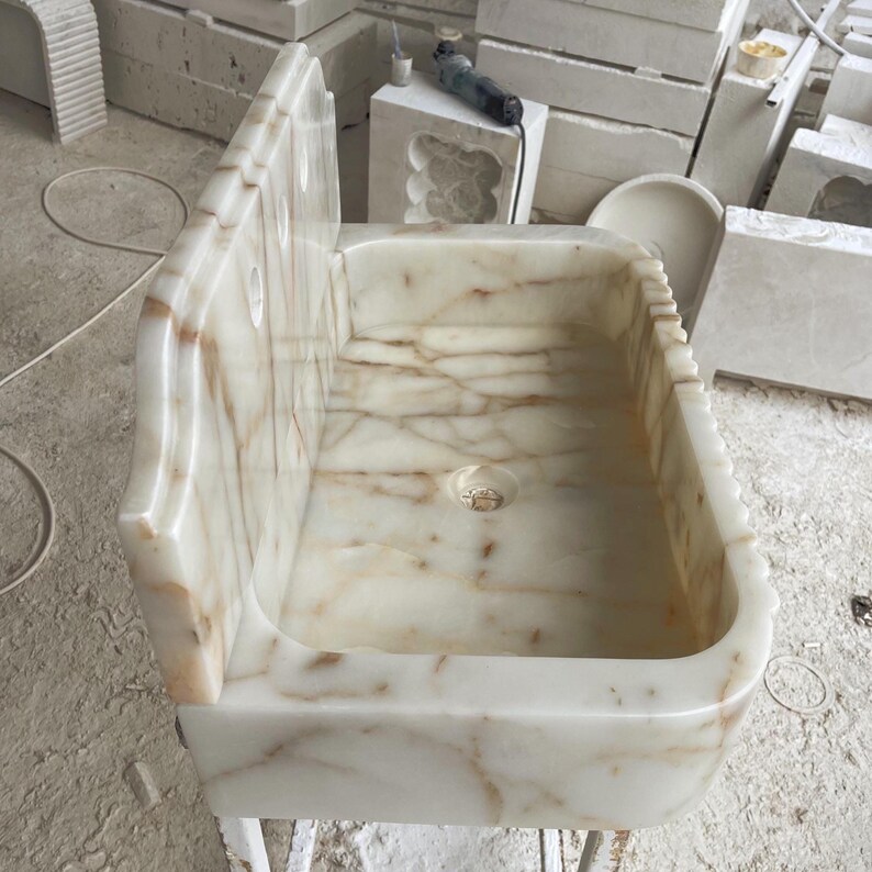 This luxurious Calacatta Gold marble sink with a back panel features a standard drain hole and a striking, elegant design with prominent grey and yellow veins on the front. It can be wall-mounted or countertop-mounted. The front has a fluted design.