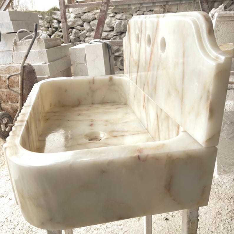 This luxurious Calacatta Gold marble sink with a back panel features a standard drain hole and a striking, elegant design with prominent grey and yellow veins on the front. It can be wall-mounted or countertop-mounted. The front has a fluted design.