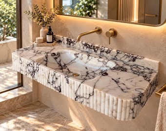 May include: A wall-mounted bathroom vanity sink crafted from white marble with prominent dark purple veining. The basin features a fluted, vertical ribbed front edge and is paired with a brushed gold wall-mounted faucet and matching handle.