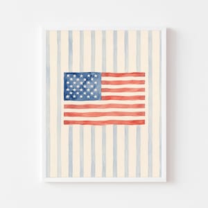 Puede incluir: Una impresión de arte mural rectangular vertical que presenta una ilustración en acuarela de la bandera de los Estados Unidos centrada sobre un fondo de rayas verticales azul pálido en una superficie de color crema, con un borde blanco.