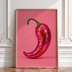 May include: A framed wall art print featuring a chili pepper covered in reflective red and pink mosaic mirror tiles. The pepper has a green stem and is set against a solid pink background, encased in a thin gold-colored rectangular frame.