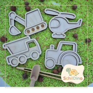 Könnte beinhalten: Holzspielzeug-Set mit Traktor, Muldenkipper, Bagger und Hubschrauber. Die Spielzeuge sind hellbraun und liegen auf grünem Reis. Ein Holzschöpfer und eine Zange sind ebenfalls enthalten. Das Logo "Schildino" ist sichtbar.