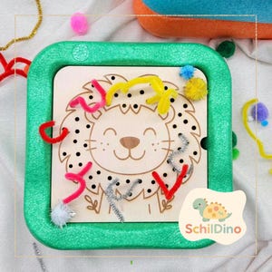 Könnte beinhalten: Ein Holz-Aktivitätsbrett mit Löwenmotiv und grünem Rahmen. Das Brett zeigt ein lächelndes Löwengesicht, Löcher und bunte Pfeifenreiniger. Das Brett ist für die Entwicklung der Feinmotorik und das sensorische Spiel von Kindern konzipiert.
