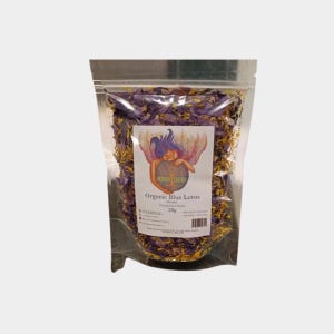Op de afbeelding: Een doorzichtige plastic zak gevuld met gedroogde blauwe lotusbloemblaadjes. De zak heeft een label met de tekst "Organic Blue Lotus" en "25g".