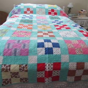 Puede incluir: Un edredón de retazos colorido con un fondo turquesa y cuadrados de varios patrones y colores, incluyendo rojo, azul, rosa y marrón. El edredón está extendido sobre una cama, mostrando su diseño hecho a mano y estética vintage.