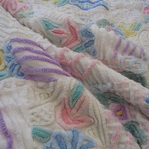 May include: A white chenille bedspread featuring a raised, tufted floral and abstract pattern in pastel shades of pink, blue, yellow, lavender, and mint green. The fabric has a soft, textured surface with intricate, looped embroidery.