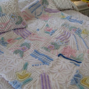 Puede incluir: Juego de colcha y almohada blancos con diseños florales y geométricos en tonos pastel. El edredón presenta bordados en relieve en rosa, azul, amarillo y lavanda. El diseño general es una mezcla de patrones florales y geométricos.