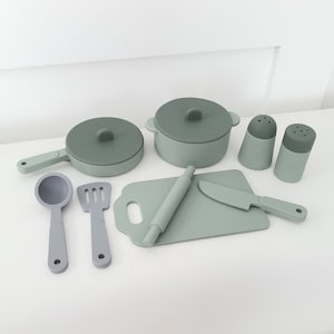 May include: A set of green silicone kitchen play food, including a rolling pin, a knife, a spatula, a ladle, two pots, and two salt and pepper shakers. The play food is designed for children to learn about cooking and food preparation.