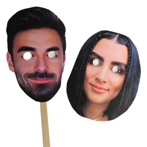 May include: Two cardboard face masks with stick handles. The masks are of a man and a woman with eye holes cut out. The man has a beard and the woman has long black hair.