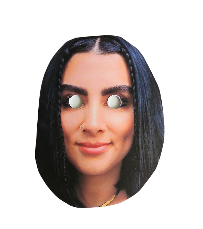 May include: A paper face mask featuring a photo of a woman with long black hair. The mask has eye holes and a nose hole.