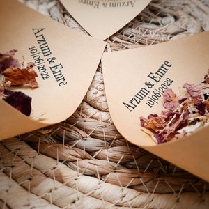 May include: Light brown paper cones filled with dried flower petals. Each cone is printed with the black text Arzum & Emre and the date 10/06/2022. The cones are arranged in a circular pattern, showcasing the natural texture of the paper.