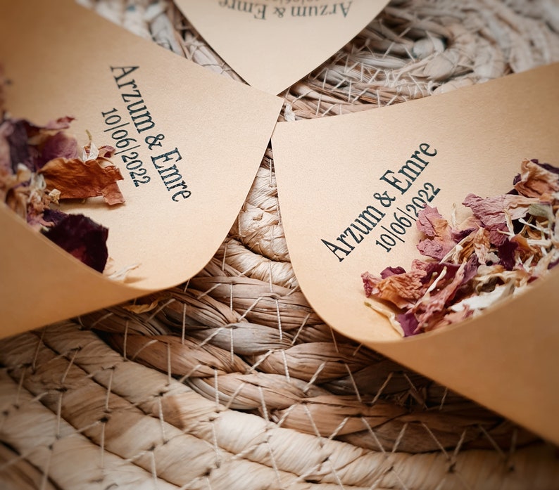 May include: Light brown paper cones filled with dried flower petals. Each cone is printed with the black text Arzum & Emre and the date 10/06/2022. The cones are arranged in a circular pattern, showcasing the natural texture of the paper.