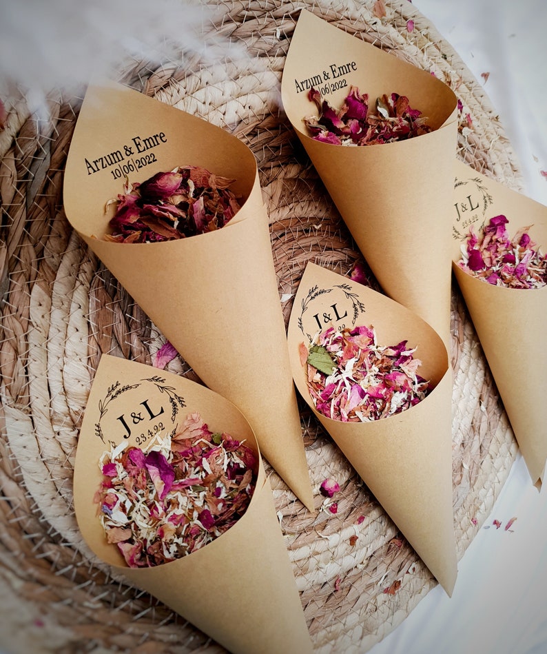 May include: Four conical paper holders made of light brown kraft paper, each filled with dried flower petals in shades of pink, white, and red. Two cones are printed with Arzum & Emre 10/06/2022, and two cones feature a wreath design with J&L 23.4.22.