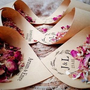 May include: Several light brown paper cones filled with dried pink, red, and white flower petals. Each cone features black printed text including names like Arzum & Emre or initials J&L, along with specific dates such as 10/06/2022 or 23.4.22.
