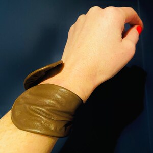 May include: A brown leather cuff bracelet with a unique folded design.