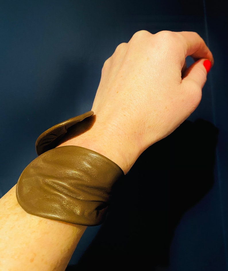 May include: A brown leather cuff bracelet with a unique folded design.