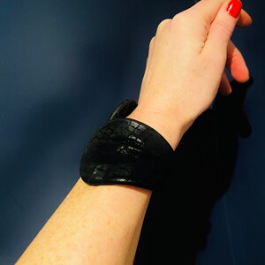 May include: A black leather bracelet with a textured surface.