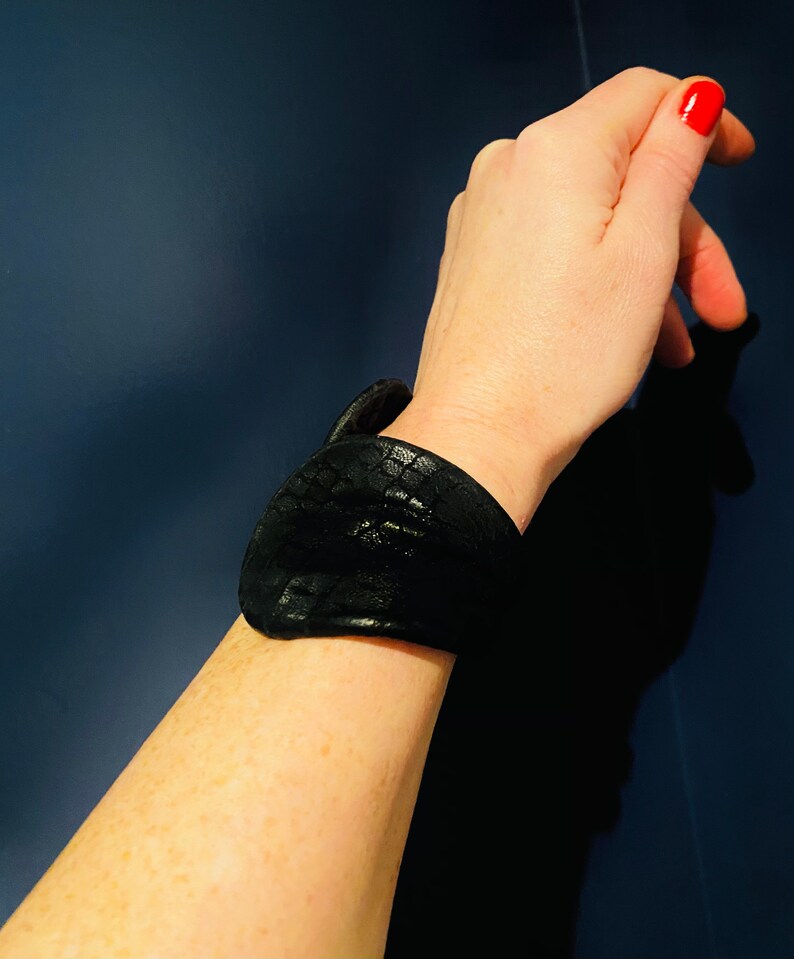 May include: A black leather bracelet with a textured surface.