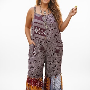 Può includere: Una tuta senza maniche dal design patchwork. La parte superiore è bordeaux scuro con un motivo geometrico e la parte inferiore presenta un patchwork di vari motivi e colori. La tuta ha tasche e bottoni decorativi.