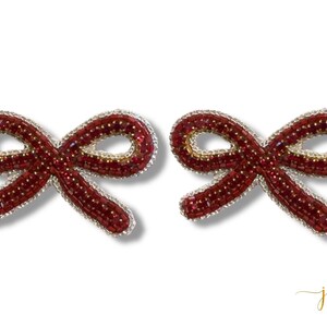 May include: Two beaded bow-shaped accessories. The bows are a deep red color with gold and silver accents. The bows are likely earrings or hair accessories.