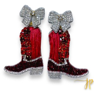 May include: A pair of red and silver boot-shaped earrings with a bow detail. The boots are embellished with red and clear rhinestones.