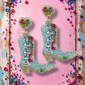 May include: A pair of turquoise beaded earrings shaped like cowboy boots. The boots have the text "Let's Go Girls" and are embellished with colorful gems. Each earring is topped with a heart-shaped accent.