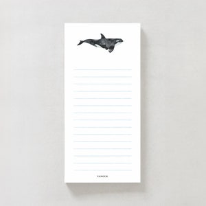 May include: A white notepad with blue lines and a black and white illustration of an orca whale. The notepad has the word "VANDUK" printed at the bottom.