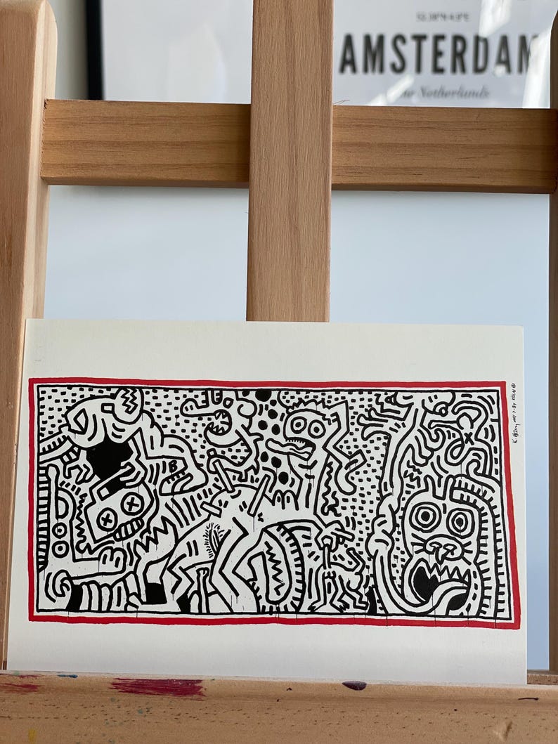 K&ouml;nnte beinhalten: Schwarz-wei&szlig;es abstraktes Kunst-Druckbild mit rotem Rand. Der Druck zeigt eine Vielzahl von Figuren und Formen, darunter eine Kreatur mit gro&szlig;en Augen und einem breiten Mund.