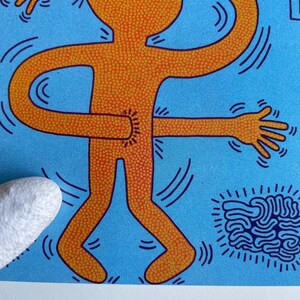 K&ouml;nnte beinhalten: Eine leuchtend orangefarbene Figur mit einem gepunkteten Muster, die in Schwarz umrandet ist, mit zwei Armen und Beinen, ist auf einem hellblauen Hintergrund dargestellt. Die Arme der Figur sind gebogen und miteinander verbunden, um einen Kreis zu bilden. Die Figur ist von schwarzen Linien umgeben, die einen wirbelnden Effekt erzeugen. Eine blaue, gehirn&auml;hnliche Form befindet sich in der unteren rechten Ecke des Bildes.