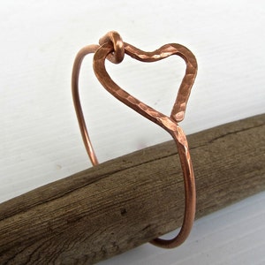 May include: A copper bracelet featuring a hammered heart design. The bracelet is open and can be adjusted to fit different wrist sizes.