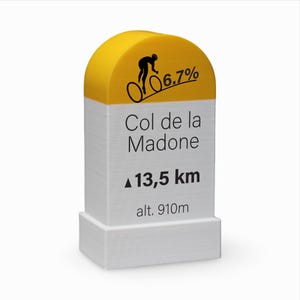 Könnte beinhalten: Ein gelb-weißer Straßenmarker mit dem Text "Col de la Madone" und "13,5 km". Der Marker zeigt auch eine Radfahrer-Grafik und "6,7%" und "alt. 910m".