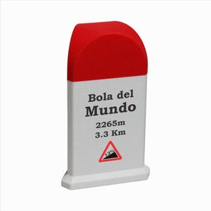 Könnte beinhalten: Ein weiß-roter Meilenstein mit der Aufschrift Bola del Mundo, 2265m und 3.3 Km. Unter dem Text befindet sich ein dreieckiges Verkehrsschild-Symbol mit einer 12%-Steigungsanzeige. Das Objekt hat eine abgerundete Oberseite und einen flachen Sockel.